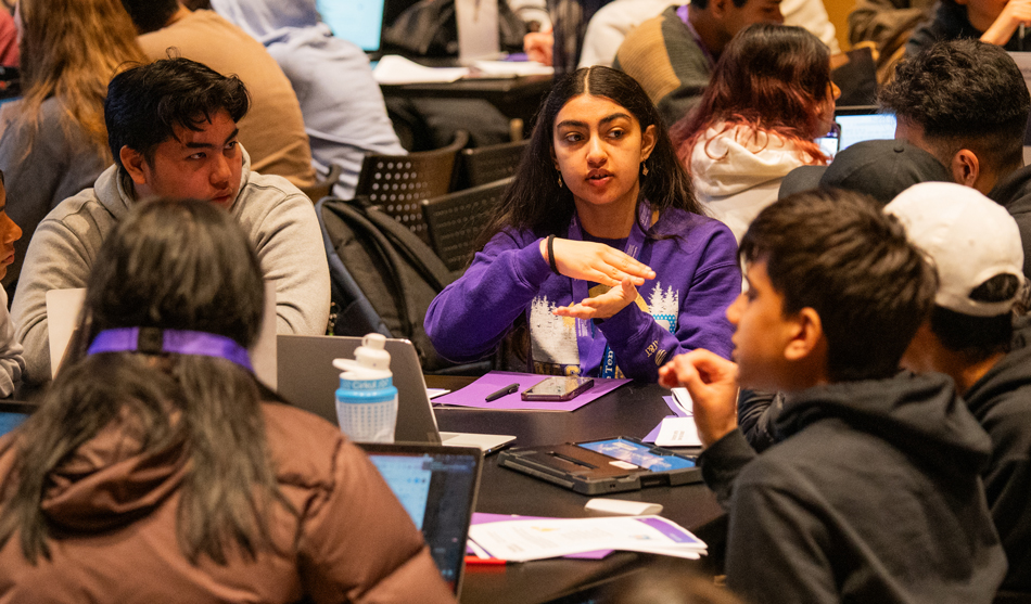 A student mentor speaks with kids participating in the Hack for Social Good hackathon.